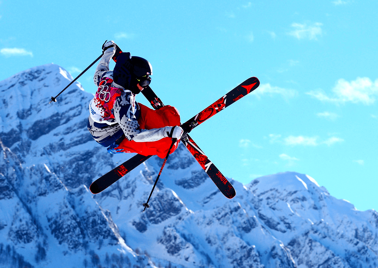 skiers in the air doing freestyle tricks with mountains in background